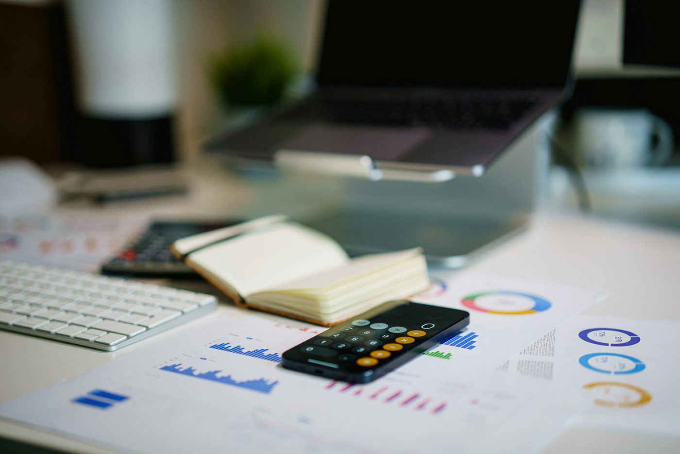 Financial reports, charts, and a calculator on a desk beside a laptop